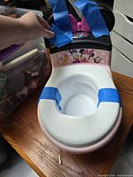 Front view of pink and white Minnie Mouse training potty with blue painters tape securing seat