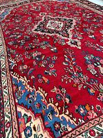 Angled close-up of rug showing red field, sky-blue guard border, floral motifs
