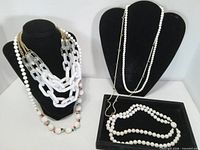 All seven white necklaces displayed on two busts and a tray