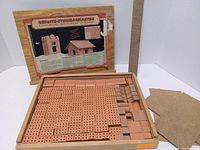 Open wooden box showing sorted miniature terracotta bricks and separate instruction panel