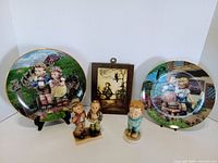 Front view of all items: two plates on stands, three figurines, wood plaque