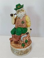 Front view of bisque musical figurine showing Santa in green attire, pipe, shamrocks