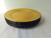 Stack of six gold lacquerware charger plates with black edges