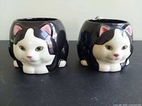 Front view of both tuxedo cat mugs showing facial details and overall shape