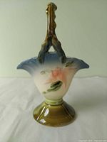 Front view showing pink flower, blue rim gradient, branch handle, pedestal base
