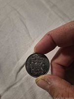Reverse of Canada 50-cent Golden Jubilee coin held between fingers, showing Canadian coat of arms