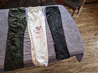 Three pairs pants laid flat: olive distressed jeans, cream joggers, black skinny pants