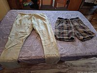 Both clothing items laid flat: beige/light olive sweatpants left, multicolor plaid shorts right