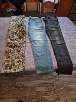 All three pairs laid flat: camo cargo, light blue denim, dark wash denim