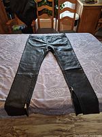 Front view of black faux leather pants laid flat showing overall style and ankle zippers