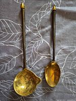 Top view of brass ladle and serving spoon showing gilt bowls and tapered handles