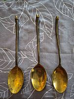 Three brass serving spoons laid out showing bowls and handles