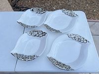 Four matching white serving bowls with silver scroll rims on table