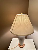 White ceramic table lamp with pleated beige shade on white table