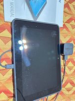 Tablet front view with charger block, cable and manual visible