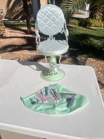 Front view of mint green doll salon chair on pedestal with accessories displayed on cape