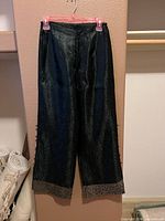 Front view of black wide-leg pants showing fabric texture and gilt trim at hem