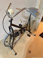 Left side view of black stationary exercise bike showing frame, front wheel, pedals, handlebar, and seat