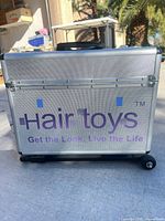 Front view of silver rolling case showing Hairtoys branding and wheels