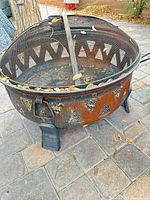 Full view of round steel fire pit with mesh cover and leaves inside