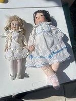 Two porcelain head cloth body dolls side by side on table
