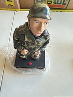 Full view of soldier figurine on base showing uniform, helmet and red button