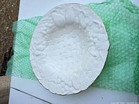 Top view of white porcelain bowl showing basketweave interior, relief fruit and gold-trimmed rim