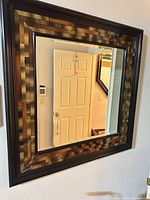 Square wall mirror hanging on wall showing reflective surface and decorative frame pattern