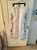 Full view of white jeans hanging showing gold trim