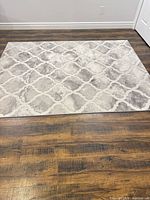 Full view of 5x7 rectangular gray/beige/cream trellis rug on hardwood floor