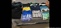 Full lot of folded boys size 10-12 tops laid out on bed