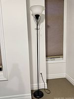 Full view of black metal torchiere floor lamp with frosted glass shade