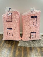 Two sealed bags of pink packing peanuts standing on floor