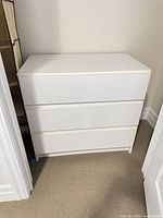 Front view of white three-drawer laminate dresser showing overall condition