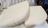 Two off-white curved seat cushions on table showing upholstery and shape