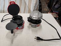 Red and silver breakfast sandwich makers, lids open, cords visible