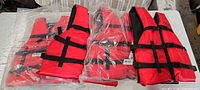 Four red life jackets on table, two sealed in plastic, two unwrapped