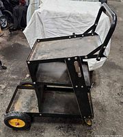 Left side view showing entire black steel MIG welder cart, three shelves, rear wheels