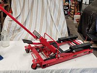 Overall view of red hydraulic motorcycle jack with handle and casters