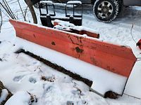 Front view of full width orange snow plow blade with snow cover