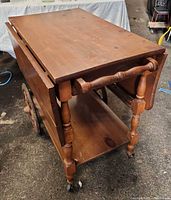 Full view of trolley, leaves down on near side, showing handle, legs, wheels and lower shelf