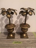 Front view of both matching brass palm tree candle holders on plinth bases