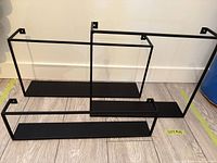Front view of three matte black CB2 floating shelves showing sizes and design
