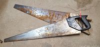 Both vintage hand saws—black plastic handle saw on top of wood handle saw—showing full blades and handles with rust and wear