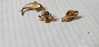 Front view of three gold-tone pins: dolphin, flower with rhinestones, leaf with pink enamel