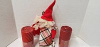 Rear view of fabric holiday gnome figure flanked by two red ribbed pillar candles