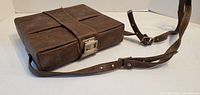 Closed rectangular brown leather camera case, strap and buckle visible