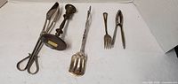 All five metal items laid out: tongs, candlestick, serving scoop, fork, nutcracker