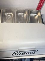 Bread box front view with three stainless pans positioned above