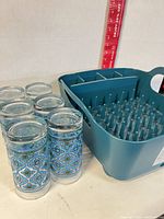 six patterned glasses beside teal dish rack